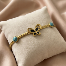 Gold bracelet with butterfly and turquoise stones on a beige cushion