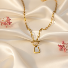 Gold Plated Iconic Toggle Pendant with a pendant on a satin surface with pink flowers