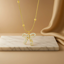 Gold necklace with a bow pendant on a marble surface