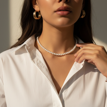 Woman wearing a pearl necklace and gold hoop earrings with a neutral background