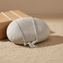 Silver hummingbird pendant necklace placed on stone with sandy background for natural look